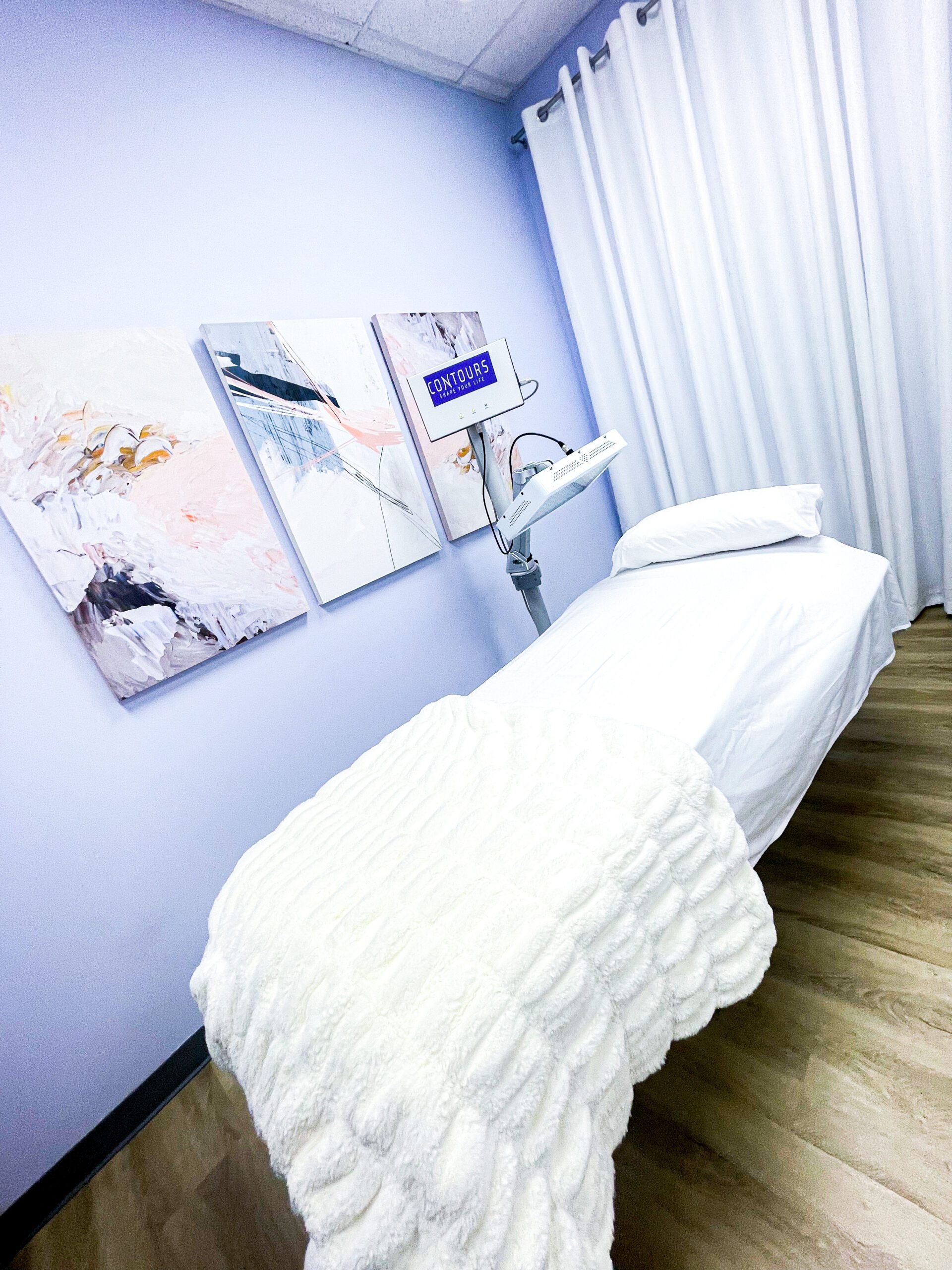A patient room containing an examination table with all white linens and pillow and a red light therapy device.